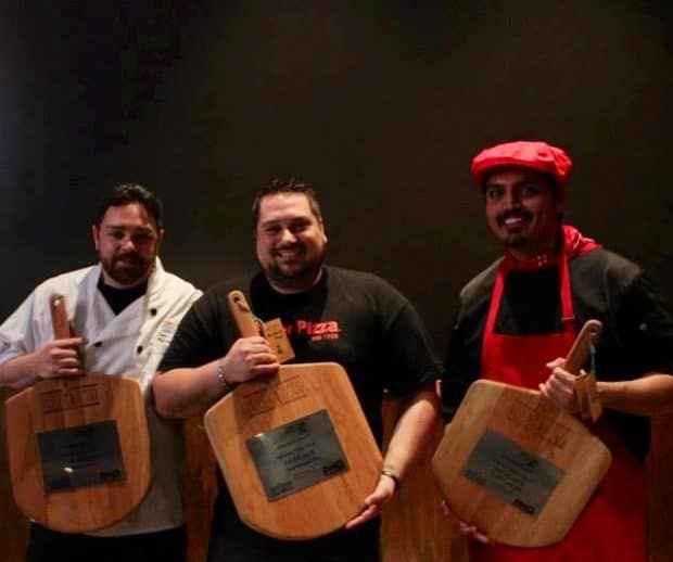 786° Degrees three members from 786 degrees standing and holding their pizza pans which are engraved with special lettering as a trophy for their win at the Pizza Competition